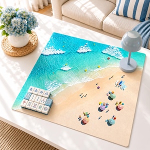 May include: A square mahjong mat featuring a high-resolution aerial view of a sandy beach with turquoise ocean waves, colorful umbrellas, and surfboards. A set of white mahjong tiles with black and red characters is arranged in the bottom left corner.