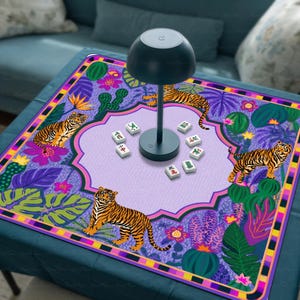 May include: A square game mat featuring a purple and green jungle pattern with tigers, cacti, and tropical flowers. A black mushroom-shaped lamp sits in the centre, surrounded by eight white mahjong tiles with black and red Chinese characters.