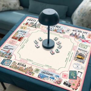 May include: A square mahjong mat featuring a travel-themed design with illustrations of Paris, London, Chicago, New York City, San Francisco, Portugal, Rome, and Santorini. A dark blue mushroom-shaped lamp sits in the center with scattered mahjong tiles.