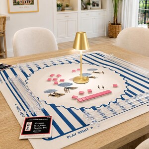 Puede incluir: Un tapete de mahjong cuadrado con borde de rayas azules y blancas y una escena de playa central con sombrillas y figuras. Incluye cuatro soportes de acr&iacute;lico transparente, fichas rosas, una l&aacute;mpara de mesa dorada y una tarjeta de reglas.
