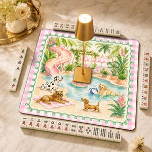 Peut inclure: Un tapis de mah-jong carré orné d'une illustration colorée de chiens au bord d'une piscine avec un toboggan rose, entouré d'une bordure à carreaux roses et blancs. Une lampe dorée est placée au centre, entourée de tuiles de mah-jong blanches.