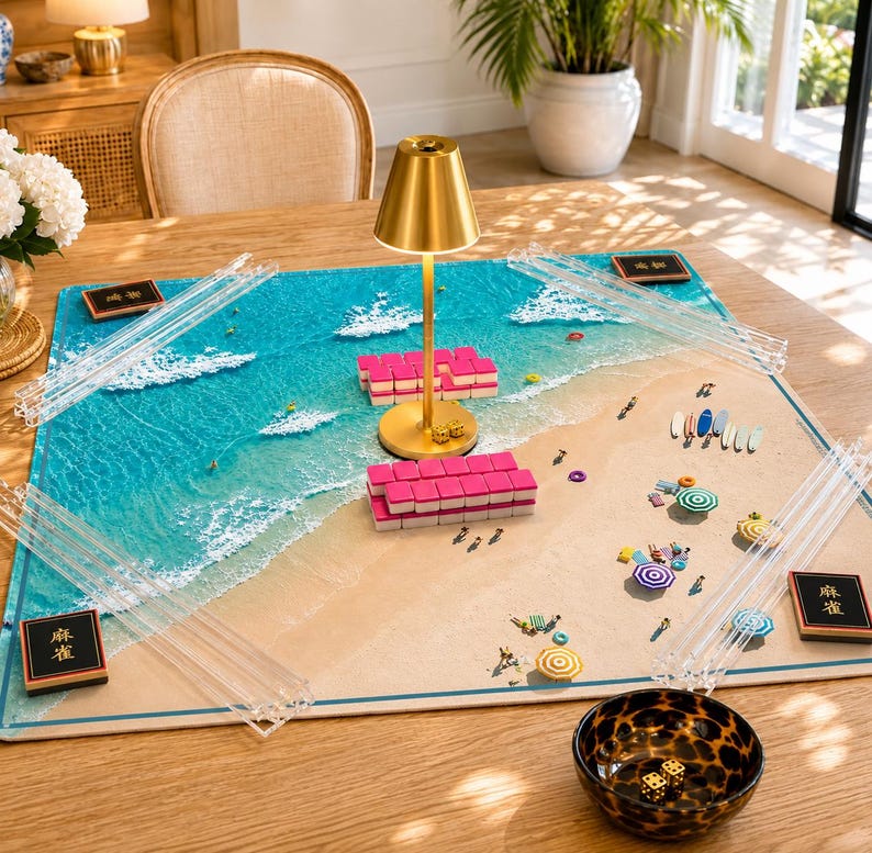 May include: A rectangular mahjong mat featuring a beach and ocean scene with turquoise water and white foam waves. The mat includes four clear acrylic tile racks, two black tiles with gold text, a gold lamp, pink tiles, and a leopard print bowl with dice.