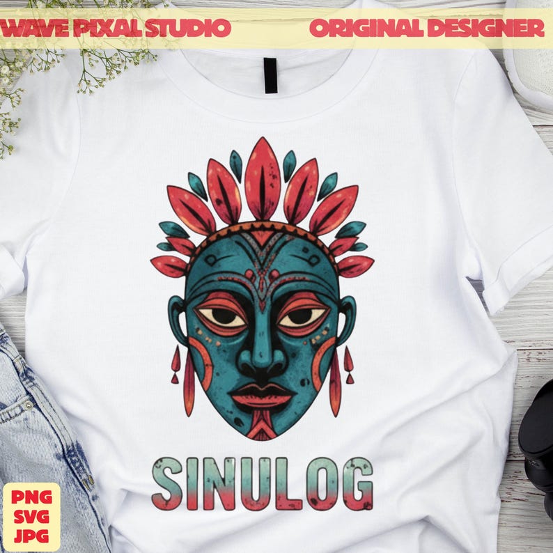 May include: White t-shirt featuring a teal and red tribal mask design with the word "SINULOG" in a colorful font. The mask has intricate details and is adorned with feather-like elements.
