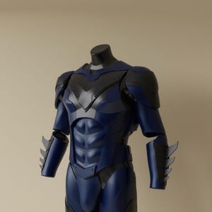 Puede incluir: Un traje de superhéroe azul y negro exhibido en un maniquí. El traje presenta un pecho y abdomen moldeados, con detalles esculpidos. Los hombros y la parte superior de los brazos son negros, y los antebrazos tienen aletas estilizadas. El diseño general es elegante y moderno.