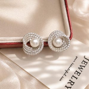 Freshwater pearl and cubic zirconia bridal stud earrings displayed on an ivory velvet jewelry box with soft champagne silk background.