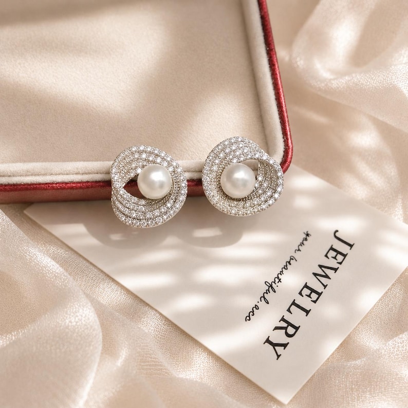 Freshwater pearl and cubic zirconia bridal stud earrings displayed on an ivory velvet jewelry box with soft champagne silk background.