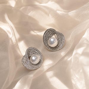 Sparkling pearl stud earrings resting on soft ivory tulle fabric in natural light.