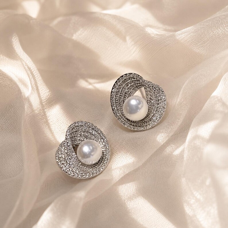 Sparkling pearl stud earrings resting on soft ivory tulle fabric in natural light.