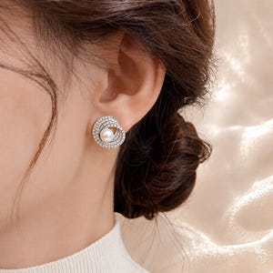 Close-up bridal model wearing freshwater pearl and cubic zirconia earrings against a soft ivory background.