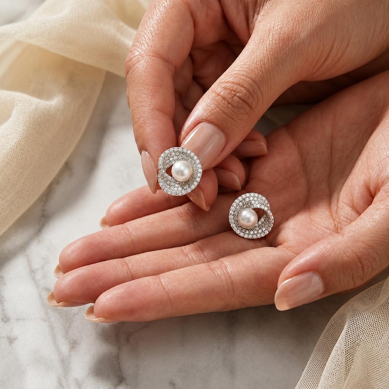 Hand holding freshwater pearl stud earrings showing size, sparkle, and intricate zirconia details.
