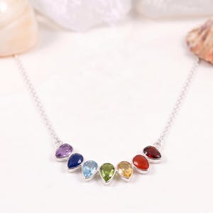 Puede incluir: Un collar de plata con siete piedras preciosas en forma de lágrima en colores del arcoíris: morado, azul, celeste, verde, amarillo, naranja y rojo. Las piedras están engastadas en biseles individuales de plata y dispuestas en curva.