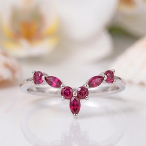 Può includere: Un anello d'argento con un design curvo, incastonato con più pietre preziose rosse ovali e rotonde. Le pietre sono disposte in un motivo floreale o a forma di foglia, creando un aspetto delicato ed elegante. L'anello è probabilmente in argento sterling.
