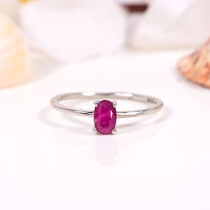 Op de afbeelding: Een zilveren ring met een ovale robijn. De robijn heeft een dieprode kleur en is gezet in een slanke, elegante band. De ring wordt gepresenteerd op een witte ondergrond, waardoor de kleur van de edelsteen wordt benadrukt. Eenvoudig, klassiek ontwerp.