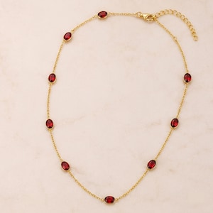 Pode incluir: Um colar de corrente dourada com oito pedras granadas de cor vermelho profundo, de corte oval, espaçadas uniformemente em engastes dourados. O colar inclui uma corrente de elos finos e um fecho lagosta com uma corrente extensora ajustável.