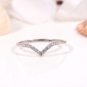 Puede incluir: Un anillo en forma de V de tono plateado que presenta una serie de pequeñas piedras transparentes de corte redondo engastadas a lo largo de la mitad superior de la banda. La banda tiene un acabado metálico pulido y una silueta en chevron.
