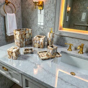 Puede incluir: Juego de accesorios de baño con un patrón único similar a la piedra en tonos marrón, beige y gris. El juego incluye un cesto de basura, una caja de pañuelos, un dispensador de jabón, un vaso, una bandeja y un jabonera. Grifería dorada.