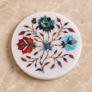 May include: A circular white marble coaster featuring an intricate floral inlay design. The pattern consists of three large blossoms in shades of deep red, dark green, and light blue, surrounded by delicate stems, leaves, and small buds in various colours.