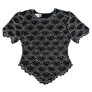 May include: Black beaded top with a scalloped hem and short sleeves. The top features a pattern of white beads, forming a fan-like design. The neckline is round, and the sleeves have a slight puff. The top is a vintage style.