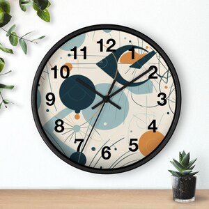 Puede incluir: Reloj de pared redondo con marco negro. La esfera tiene un fondo crema con formas abstractas azules, naranjas y azul marino. Las manecillas y los números negros completan el diseño. El reloj está sobre una superficie de madera.