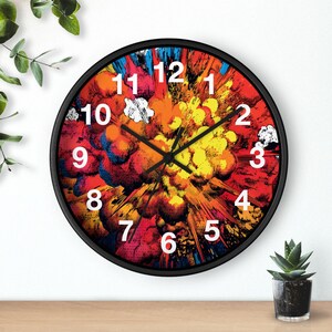 May include: A round wall clock with a black frame. The clock face features a colorful, abstract design resembling an explosion, with shades of red, yellow, and blue. White numbers mark the hours.