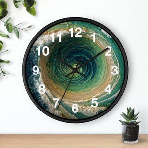 Peut inclure: Une horloge murale ronde avec un cadre noir. Le cadran présente un motif abstrait tourbillonnant dans des tons de vert, de bleu et de beige. Des chiffres blancs indiquent les heures. Les aiguilles de l'horloge sont noires.
