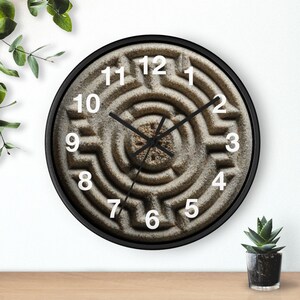 May include: Round wall clock with a black frame. The clock face features a textured, maze-like design in shades of brown and tan. White numerals mark the hours, and black hands indicate the time. A decorative piece for any room.