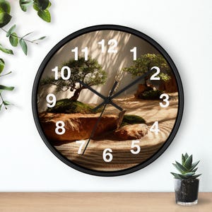 Pode incluir: Um relógio de parede redondo preto com um design de jardim zen. O mostrador do relógio exibe uma paisagem serena com árvores em miniatura, rochas e areia rastelada. Os algarismos brancos marcam as horas e os ponteiros pretos indicam as horas.