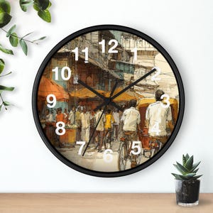 Könnte beinhalten: Eine runde Wanduhr mit schwarzem Rahmen. Das Zifferblatt zeigt eine Straßenszene mit Menschen, Fahrrädern und Marktständen. Weiße Ziffern markieren die Stunden. Schwarze Zeiger zeigen die Uhrzeit an.