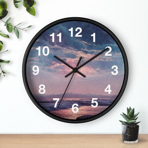 May include: A round wall clock with a black frame. The clock face features a scenic image of a sunset over the ocean, with white numerals marking the hours. Black hands indicate the time.