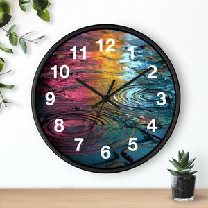 May include: A circular wall clock with a black frame. The clock face displays a colourful water ripple design with white numerals. The clock hands are black.