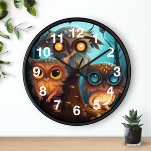 Puede incluir: Un reloj de pared redondo con marco negro. La esfera muestra una ilustración caprichosa de tres búhos con ojos grandes. El fondo es azul y verde. Las manecillas del reloj son negras y los números blancos.