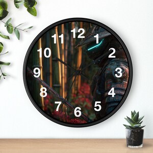 Op de afbeelding: Een ronde wandklok met een zwart frame. De wijzerplaat toont een gedetailleerde afbeelding van een futuristische krijger in een bamboebos. Witte cijfers markeren de uren. Een kleine potplant staat eronder.