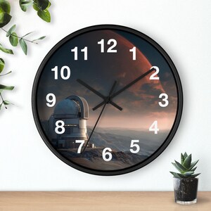 May include: A round wall clock with a black frame. The clock face features a celestial scene with a planet, observatory, and white numerals. The clock hands are black.