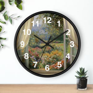 May include: A circular wall clock with a black surround. The clock face depicts a garden scene seen through a window with cream curtains. The clock hands are black, and the numbers are white.
