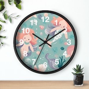Könnte beinhalten: Runde Wanduhr mit schwarzem Rahmen. Das Zifferblatt hat einen türkisfarbenen Hintergrund mit Illustrationen von Meerjungfrauen, Muscheln und Wasserpflanzen. Die Zeiger sind schwarz und die Zahlen weiß.