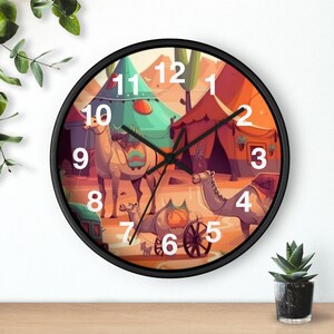May include: Round wall clock with a black frame featuring a desert scene with camels and tents. The clock face has large white numbers and black hands. The artwork is colorful with shades of orange, teal, and brown.