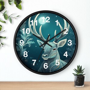 May include: A round wall clock with a black frame. The clock face features a blue deer illustration with large antlers, a full moon, and white numerals. The clock hands are black.