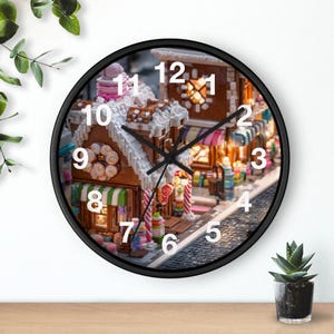 Può includere: Un orologio da parete con cornice nera con una dettagliata scena di casa di pan di zenzero. Il quadrante dell'orologio mostra numeri e lancette tradizionali, con il design della casa di pan di zenzero che include bastoncini di zucchero, caramelle colorate e un tetto innevato. L'orologio è un oggetto decorativo.