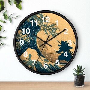 Puede incluir: Reloj de pared redondo con marco negro. La esfera presenta un diseño de inspiración japonesa con una gran ola azul, una silueta de samurái y números blancos. Las manecillas del reloj son negras.