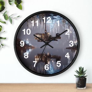 May include: A round wall clock with a black frame. The clock face features a futuristic scene with a structure over water, with white numbers and black clock hands. The clock is on a wooden surface.