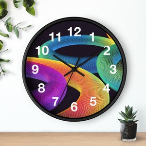Pode incluir: Um relógio de parede redondo com moldura preta e fundo escuro. O mostrador do relógio apresenta formas abstratas coloridas e giratórias em tons de azul, verde, amarelo, laranja e roxo. Os algarismos brancos marcam as horas.