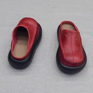 Puede incluir: Un par de zapatos sin cordones de cuero rojo con suelas negras. Los zapatos tienen una punta redondeada y un tac&oacute;n bajo. La parte superior es de color rojo intenso y las suelas son negras. Cada zapato mide unos 25 cm de largo.