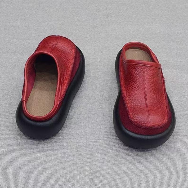Puede incluir: Un par de zapatos sin cordones de cuero rojo con suelas negras. Los zapatos tienen una punta redondeada y un tac&oacute;n bajo. La parte superior es de color rojo intenso y las suelas son negras. Cada zapato mide unos 25 cm de largo.