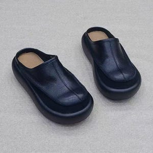 Puede incluir: Un par de zuecos negros de cuero sin cordones. Los zapatos tienen una punta redondeada y una suela gruesa de plataforma. La parte superior del zapato es de cuero liso y la plantilla es de color beige claro. Los zuecos est&aacute;n dise&ntilde;ados para la comodidad y el estilo.