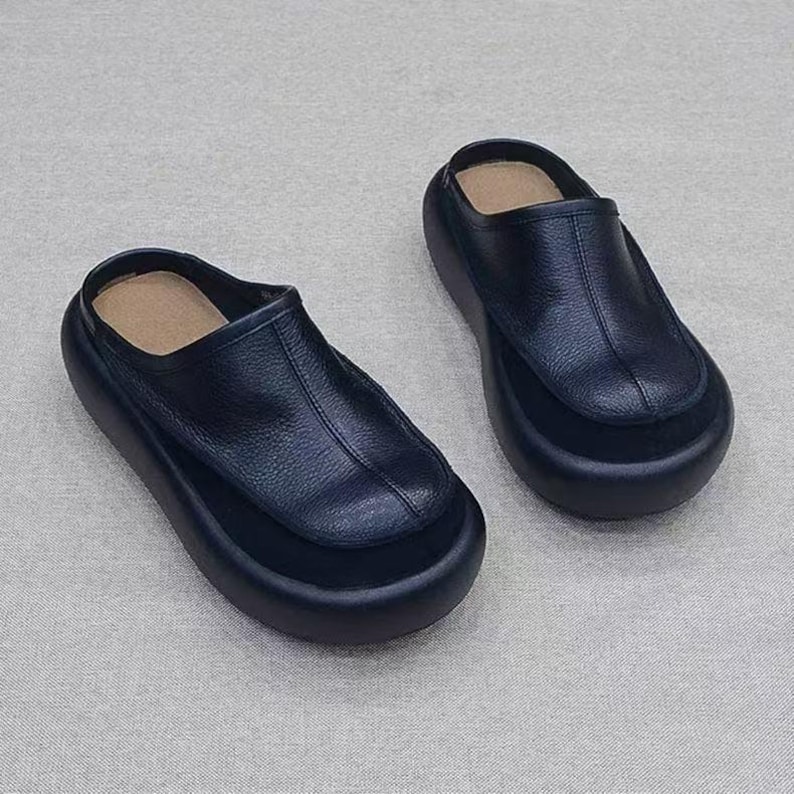 Puede incluir: Un par de zuecos negros de cuero sin cordones. Los zapatos tienen una punta redondeada y una suela gruesa de plataforma. La parte superior del zapato es de cuero liso y la plantilla es de color beige claro. Los zuecos est&aacute;n dise&ntilde;ados para la comodidad y el estilo.