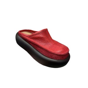 Puede incluir: Un zueco de cuero rojo con suela de plataforma negra. El zapato presenta una parte superior de cuero texturizado y un material similar al ante entre la parte superior y la suela. El zueco est&aacute; dise&ntilde;ado con la parte trasera abierta.