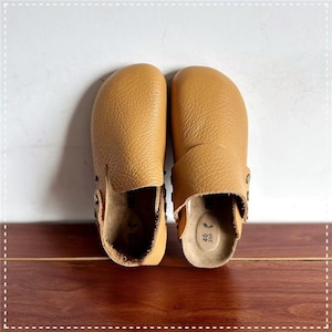 Puede incluir: Un par de zuecos de cuero color canela con un acabado texturizado. Los zuecos tienen una puntera redondeada y una correa con hebilla metálica. Las suelas son de color marrón claro con textura similar al corcho. Talla 40.