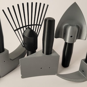 May include: A collection of gray gardening tools with black handles. The set includes a hammer, rake, trowel, corner tool, and a hoe. The tools are arranged on a white surface, showcasing their design and functionality. Ideal for gardening and landscaping.