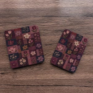 May include: Two rectangular electronic reader covers featuring a patchwork design of various floral illustrations in shades of deep purple, burgundy, and muted pink. Each cover displays a grid of squares containing different botanical motifs.