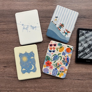 Op de afbeelding: Vier rechthoekige e-readerhoezen met verschillende ontwerpen: een witte met blauwe lijntekeningen van wasgoed, een blauw gestreepte met honden op skateboards, een crèmekleurige met een zon- en maanillustratie en een witte met een kleurrijk tropisch patroon.